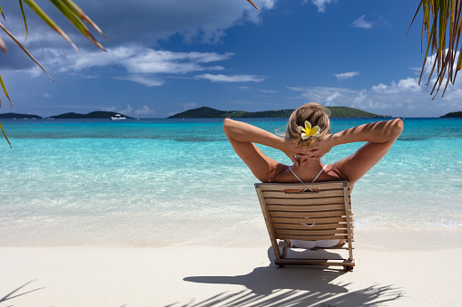 woman relaxing in teak beach chair on a tropical beach in the Caribbean