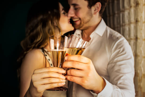 Couple celebrating New Year's Eve in the house holding with focus on their glasses. Romantic young couple cheering at New Year's Eve. kissing on the mouth stock pictures, royalty-free photos & images