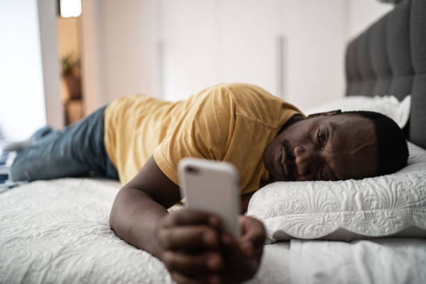 homme aîné fatigué utilisant le smartphone se trouvant dans le bâti à la maison - tired men african descent sadness photos et images de collection