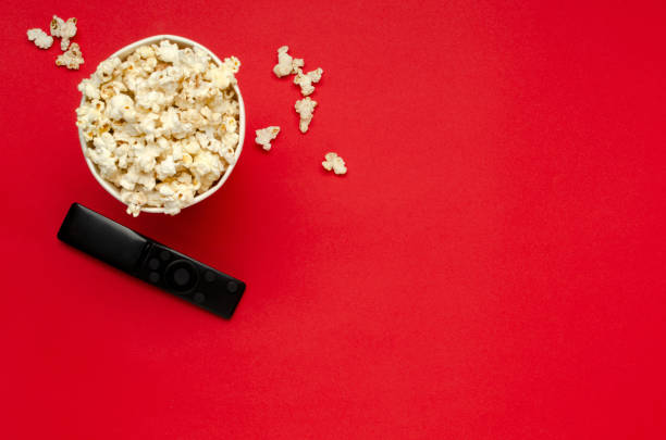 top view of paper bucket full of sweet popcorn, black tv clicker on the red background.empty space - remote television movie box imagens e fotografias de stock