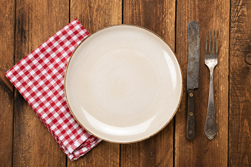 Top view of a plate with a spoon and fork at the right side shot against a wooden table background