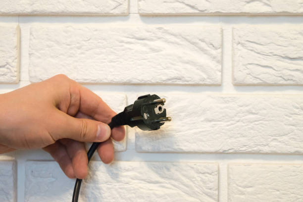 vista de uma mão segurando um plugue preto de 220v contra uma parede de tijolos brancos - 240v - fotografias e filmes do acervo