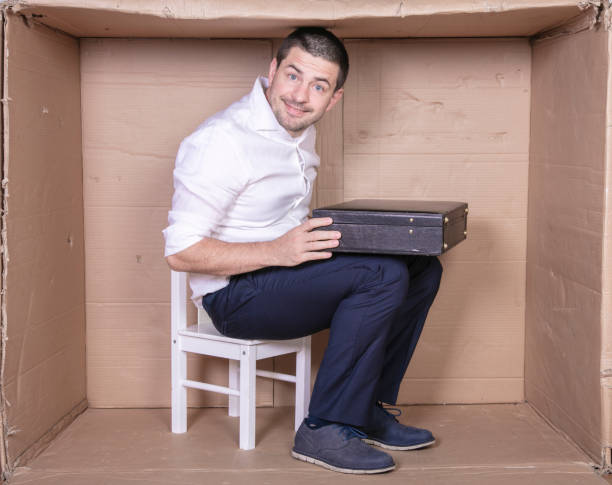 istock businessman with a briefcase sits in a tight cardboard box imitating an office 1291185217