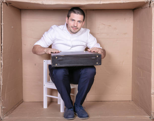 istock businessman with a briefcase sits in a tight cardboard box imitating an office 1291185245