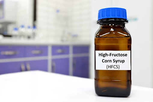 Selective focus of high-fructose high fructose corn syrup or hfcs food and beverage sweetener in dark brown glass bottle inside a laboratory.