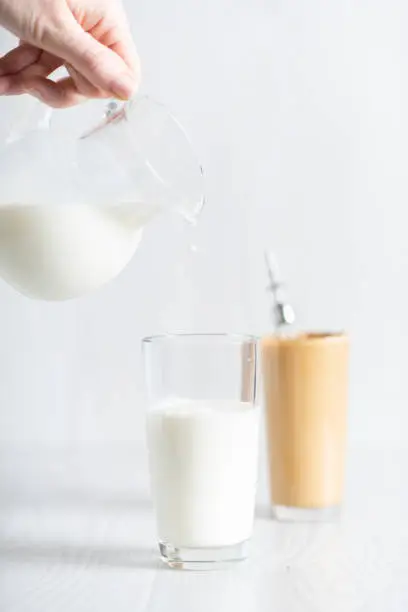 The process of making a fashionable Korean drink dalgonacoffee. Glass and decanter with milk on a light background. Milk is poured into a glass.