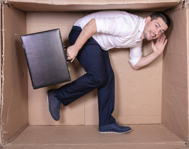 istock businessman with a briefcase sits in a tight cardboard box imitating an office 1291185486