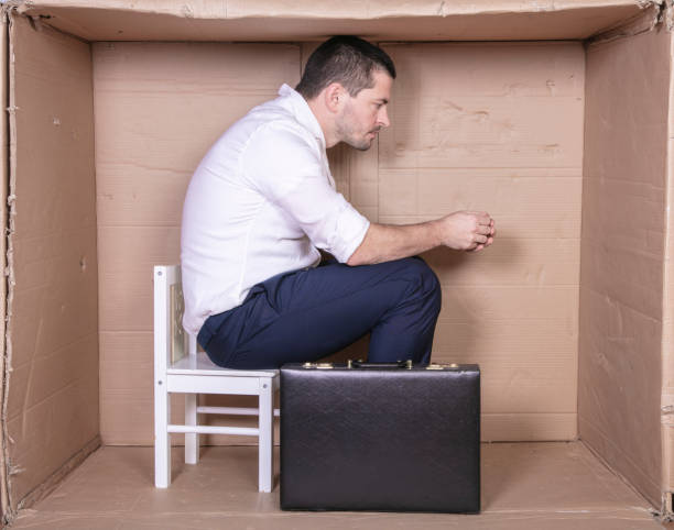 istock businessman with a briefcase sits in a tight cardboard box imitating an office 1291185511