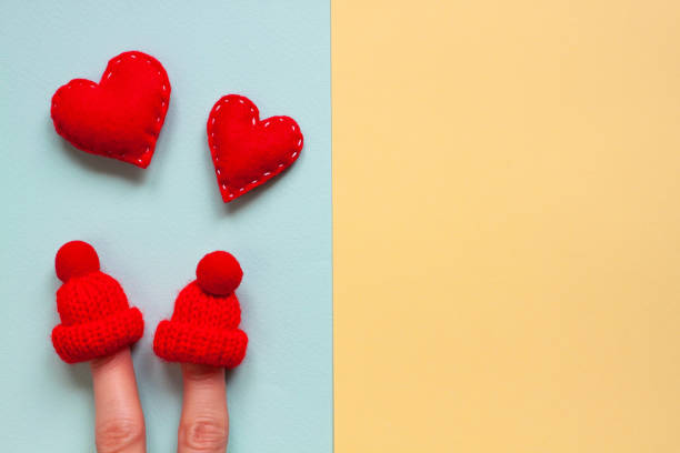 Love for two forever. Happy valentine's day creative concept on blue and yellow Image of an enamored couple of people using a female fingers. Red felt hearts and knitted winter miniature hats. felt heart shape small red stock pictures, royalty-free photos & images