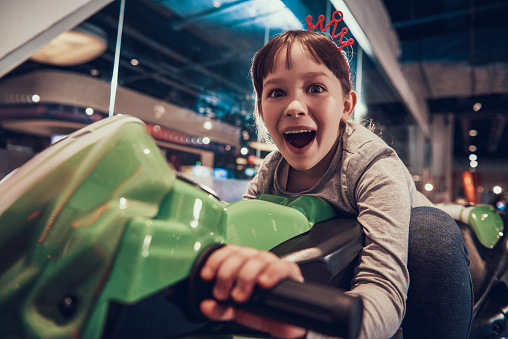 Little Girl on Toy Motorcycle in Amusement Center. Adorable Happy Child having Fun. Modern Entertainment. Childhood Concept. Cheerful Kid Riding Toy Motorbike Indoors. Excited Child.