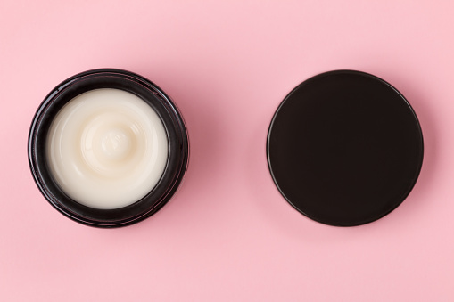 Cosmetic face cream in an open jar on a pink background.