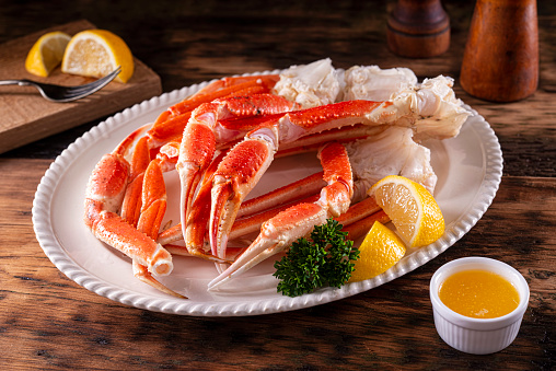 A plate of delicious snow crab leg clusters with lemon, parsley and melted butter.