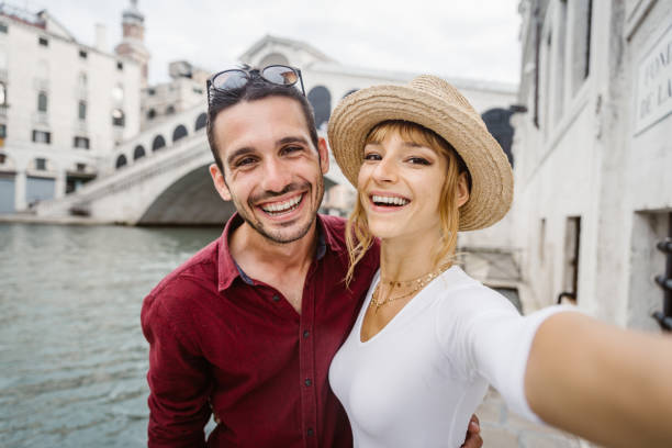 pareja romántica en el amor en las vacaciones en venecia, italia. los jóvenes se besan y se toman un selfie frente al puente de rialto. - venice italy rialto bridge italy gondola fotografías e imágenes de stock