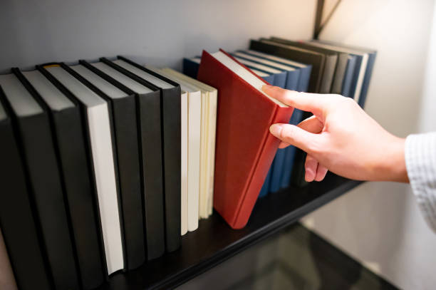 istock Male hand picking red book on bookshelf 1291207725