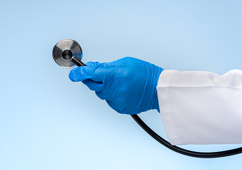 Doctor's hand wearing blue gloves is holding a stethoscope on blue background