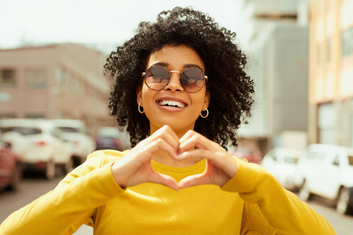 Cropped shot of a woman forming a heart shape with her hands while out in the city
