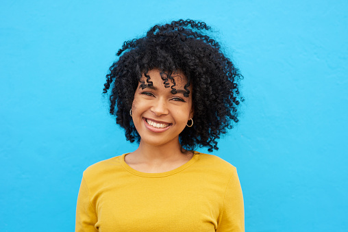 Cropped shot of a young woman looking happy while posing against a blue wall