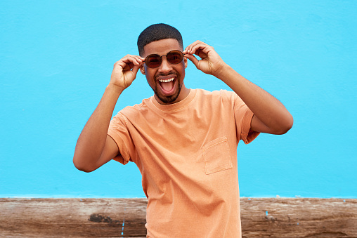 Shot of a handsome young man wearing sunglasses while posing against a blue wall