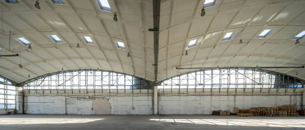 istock Huge empty industrial warehouse. White interior. Unique architecture. Hemispherical reinforced concrete load bearing roof with windows. Wooden pallets near wall. 1291208337
