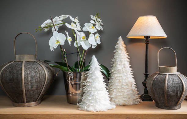Still life with white orchid, lamp, decorative trees and candle holders.