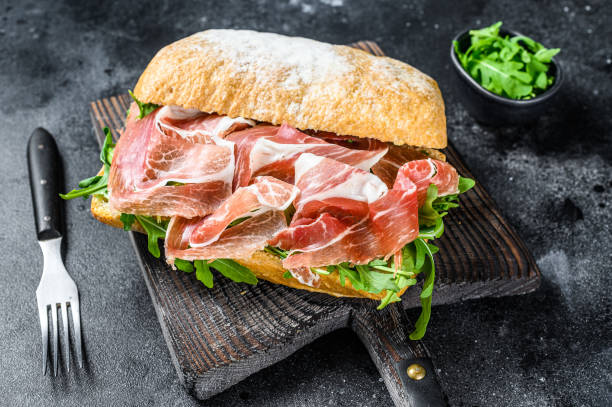 istock iberico jamon ham sandwich on ciabatta bread. Black background. Top view 1291211066