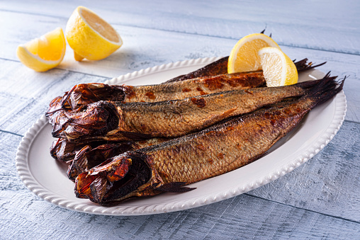 A plate of delicious smoked herring kippers with lemon on a wood table top.