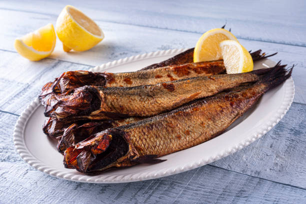 Smoked Herring Kippers A plate of delicious smoked herring kippers with lemon on a wood table top. kipper stock pictures, royalty-free photos & images