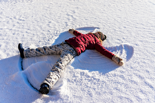 Young woman lying in the snow and making a snow angel. Winter walks and fun, holidays