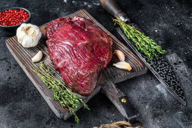istock Venison raw deer meat on a cuuting board with herbs. Black background. Top view 1291213188