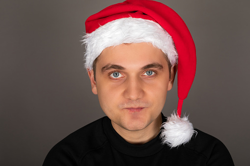 Portrait of an attractive young man wearing Santa hat, posing in front of grey background