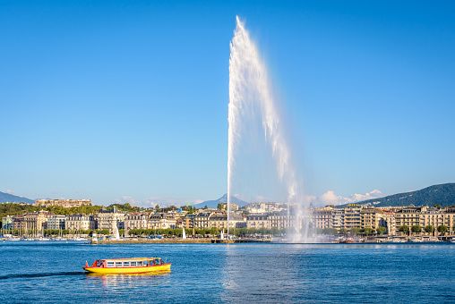 Geneva, Switzerland - September 3, 2020: A Mouettes Genevoises water bus from the M1 line is crossing the bay of Geneva on a sunny summer day with the Jet d'Eau water jet fountain in the background.