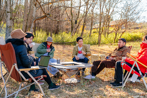 A group of friends are enjoying drinking hot drink at a camp site in the morning in winter.