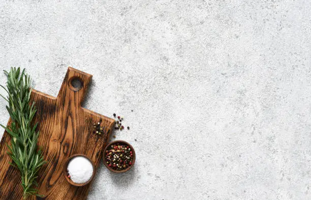 Photo of Cutting board with rosemary and spices on a light concrete background.