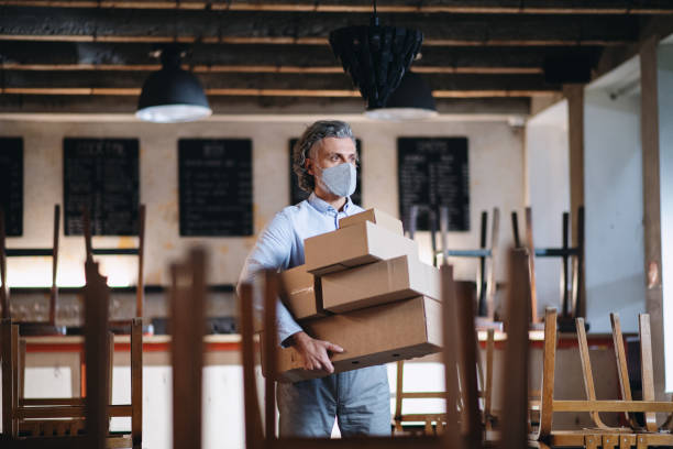 Frustrated owner carrying boxes in closed cafe, small business lockdown due to coronavirus.