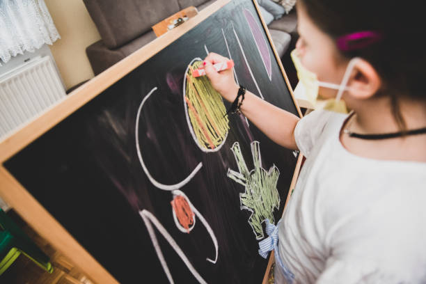 istock Cute little girl is drawing on blackboard 1291234322