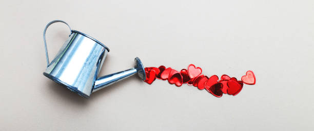 istock silver watering can pouring hearts on a light beige background. Valentines background, love, date concept 1291237227