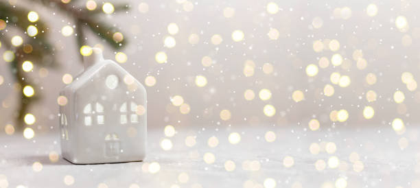 istock Small toy model house and fir branch on white table with light blurred wall background. Horizontal composition 1291237997