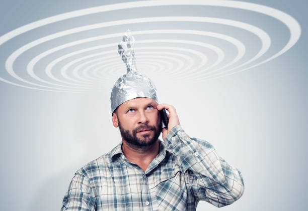 bearded funny man in an aluminum hat talking on a smartphone with the sky, taking cosmic electric waves, concept idiots - tin foil hat imagens e fotografias de stock