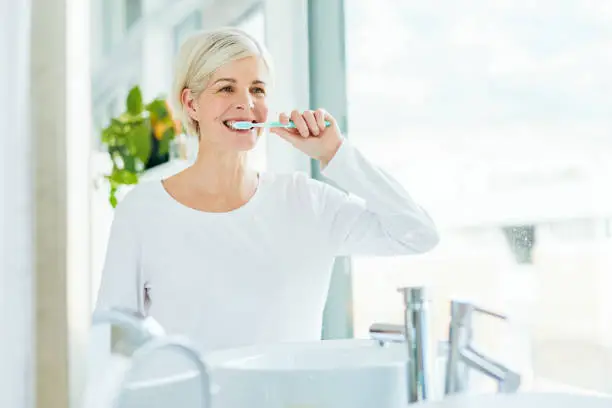 Shot of a mature woman brushing her teeth in a bathroom at home