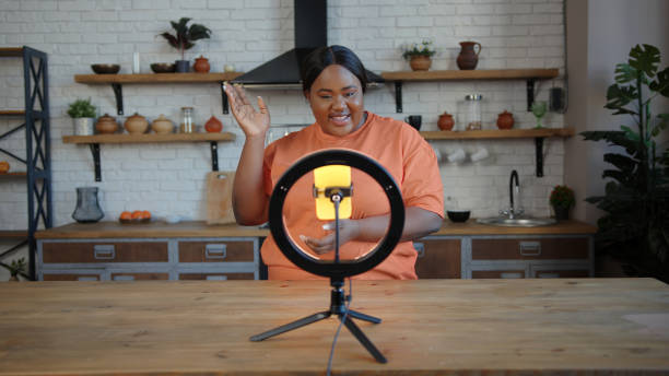 istock Plump blogger with ponytail speaks at tripod with smartphone 1291254454
