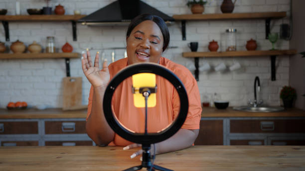 istock Plump blogger with ponytail speaks at tripod with smartphone 1291254462
