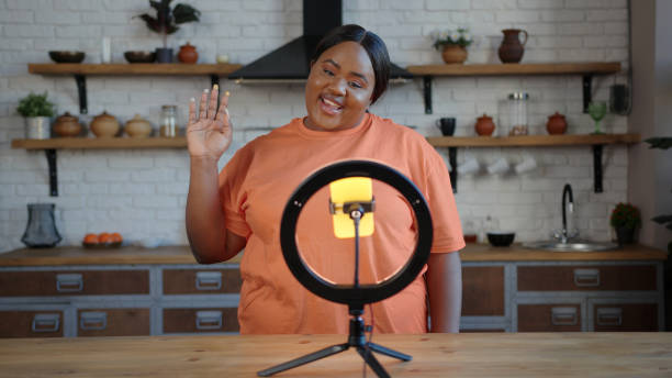 istock Plump blogger with ponytail speaks at tripod with smartphone 1291254520