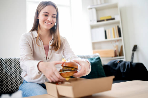 wanita muda dengan hamburger take away di rumah, coronavirus dan konsep pengiriman makanan. - home delivery potret stok, foto, & gambar bebas royalti