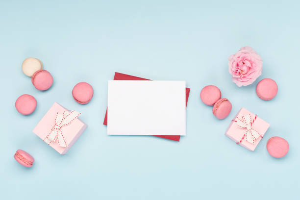 istock Valentines Day card. Pink gifts with ribbon, empty envelope and macaron macaroon cookie on blue background. 1291257182