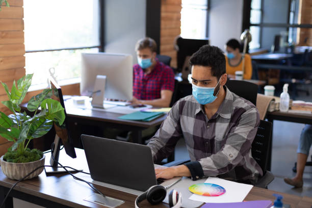 istock Diverse male colleagues wearing face masks working in computers at office desks 1291257499