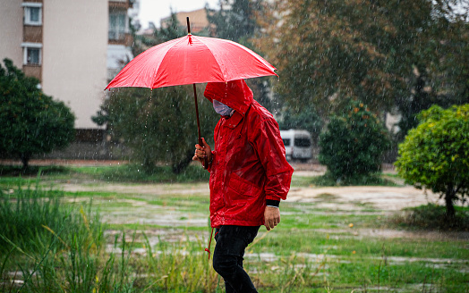 Mature man wearing red raincoat walking on city street in rain with a red umbrella