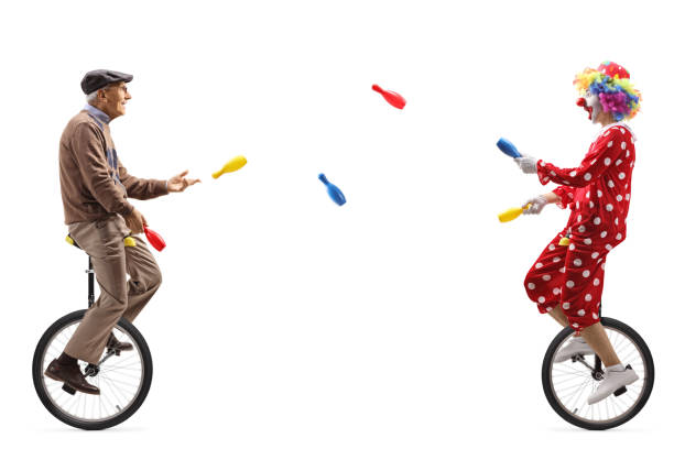 istock Elderly man and a clown riding unicycles and juggling 1291260441