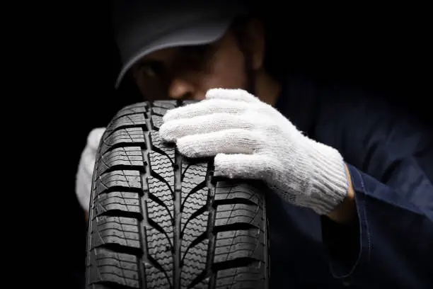 Auto mechanic checking a car tire on a black background