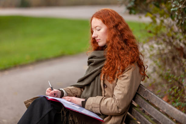 ruhige szene im stadtpark mit junger frau auf einer bank sitzend und ihre aufgabenarbeit schreibt - proofreading reading and writing writing exam stock-fotos und bilder