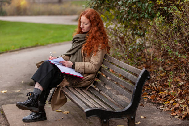 un angolo tranquillo nel parco cittadino dove una giovane donna studia su una panchina e completa qui il lavoro di assegnazione - proofreading reading and writing writing exam foto e immagini stock